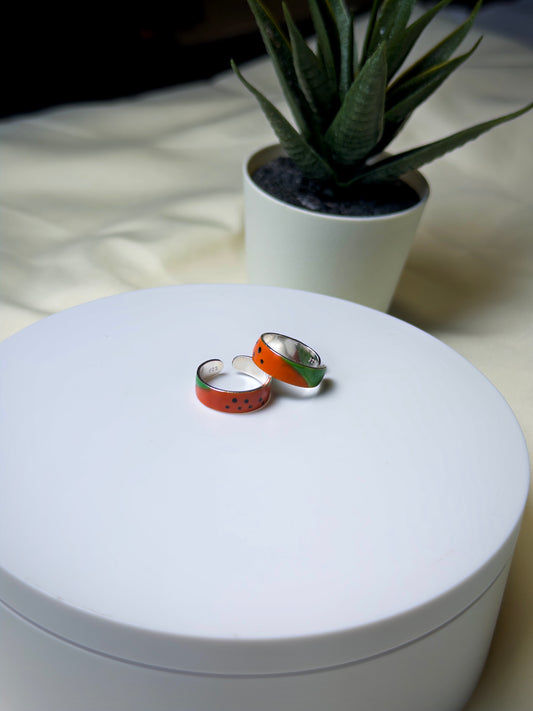 Two colorful toe rings on a white surface with a plant in the background