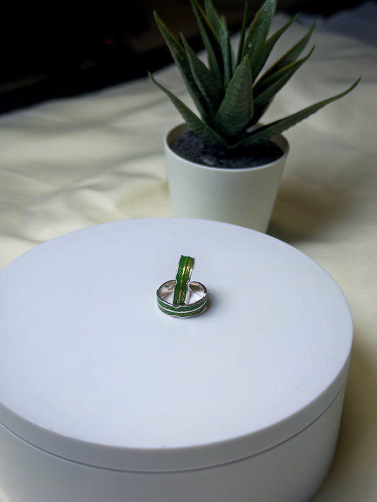 Silver toe ring with green accent on a white box, potted plant in the background