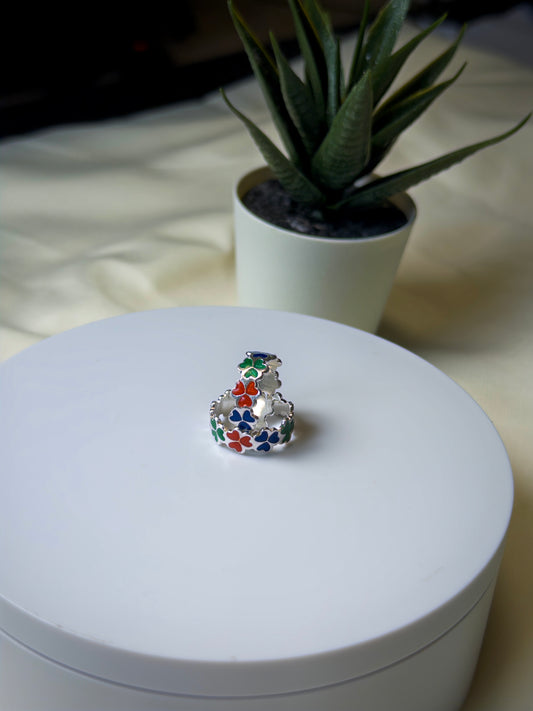 Toe ring with colorful gemstones on a white surface, with a plant in the background.