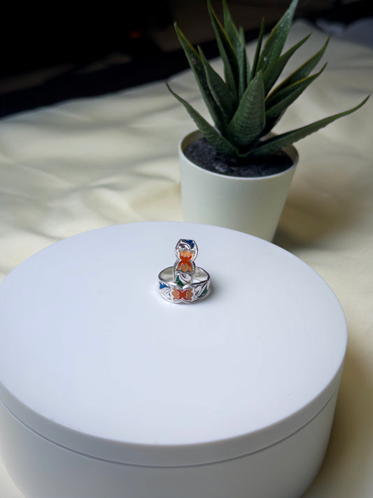 Silver toe ring with colorful design on a white box, potted plant in the background