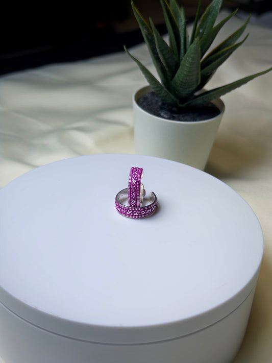 Two pink toe rings on a white surface with a plant in the background