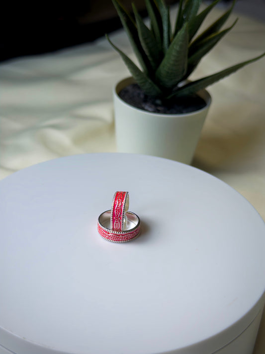 Two toe rings stacked on a white surface with a plant in the background