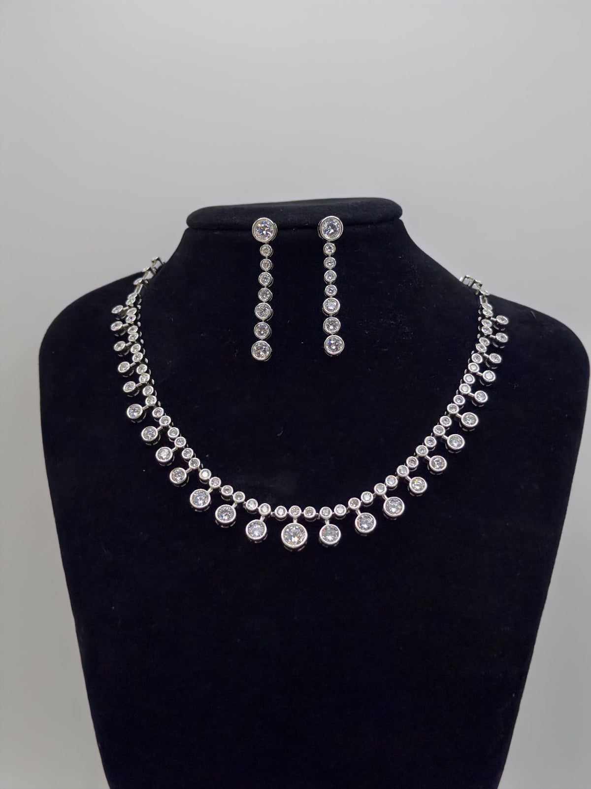 Silver necklace and earrings set on a black bust against a gray background
