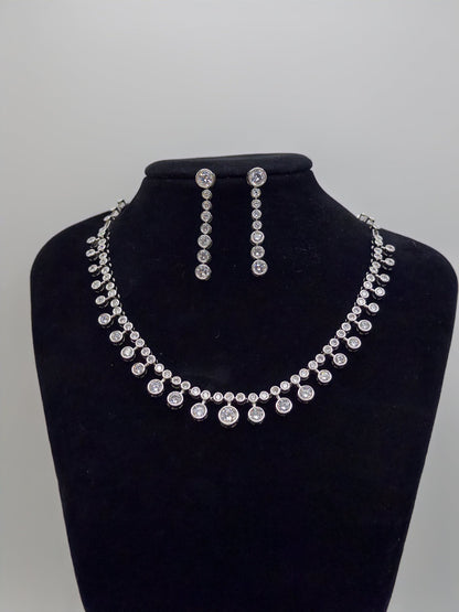 Silver necklace and earrings set on a black bust against a gray background